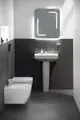 Modernes Badezimmer mit Waschbecken und Wandtoilette in weiß, graue Wandverkleidung, beleuchteter Spiegel von Ideal Standard über dem Waschbecken.